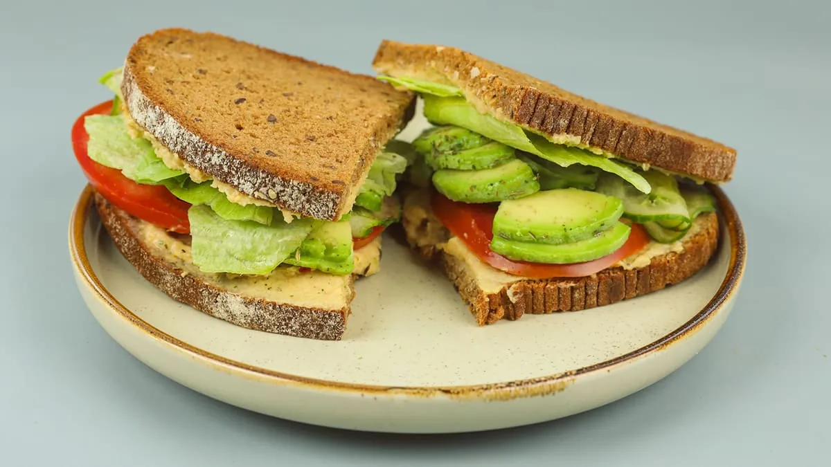 A hummus sandwich with avocado, tomato, cucumber, seeds and iceberg lettuce.